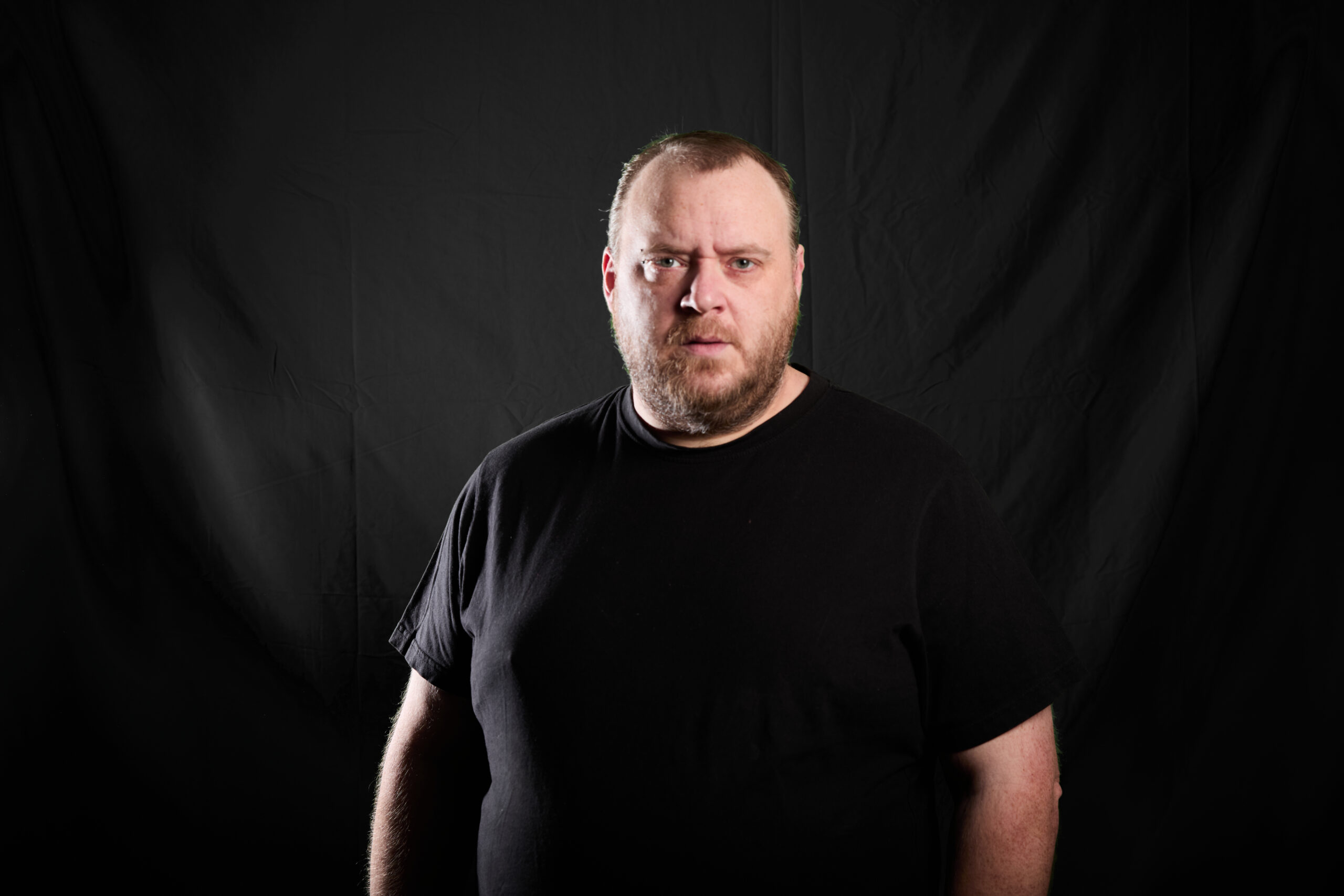 Portrait de Cédric Michaux devant un fond noir, éclairé avec des ombres marquées.